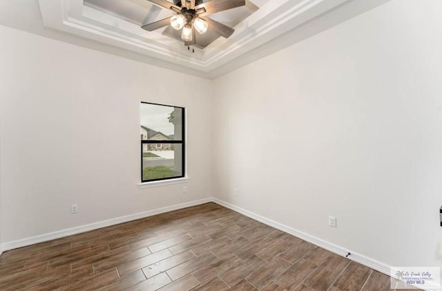 empty room with ceiling fan, wood-type flooring, and a tray ceiling