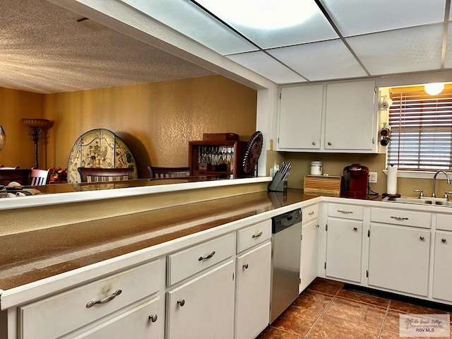 kitchen with dark tile patterned floors, dishwasher, sink, and white cabinets