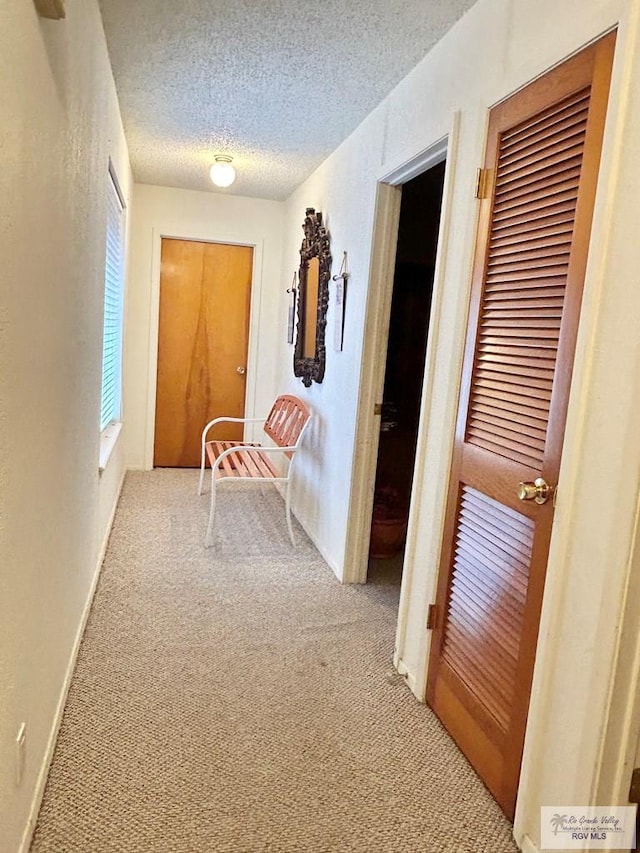 hallway with light carpet and a textured ceiling