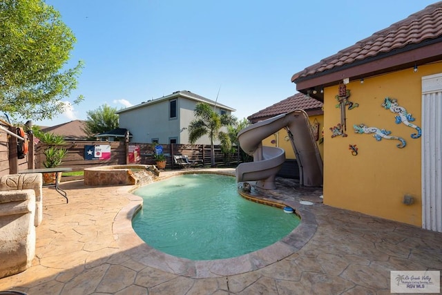 view of swimming pool with a patio area, a water slide, and an in ground hot tub