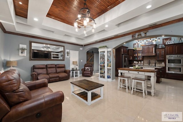 living room featuring a tray ceiling, ornamental molding, a chandelier, and wood ceiling