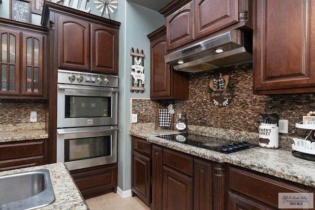 kitchen with double oven, black electric stovetop, light stone counters, and tasteful backsplash