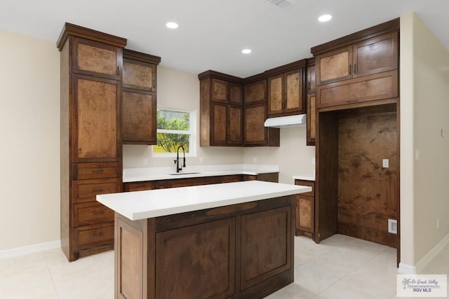 kitchen with dark brown cabinetry, sink, a kitchen island, and light tile patterned floors