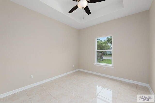 tiled spare room featuring a raised ceiling and ceiling fan