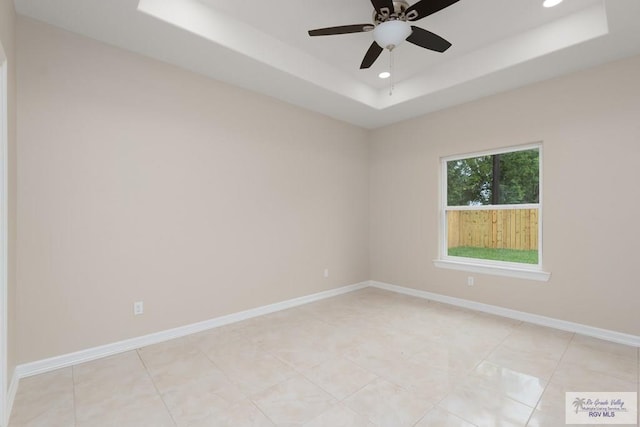 tiled empty room featuring a tray ceiling and ceiling fan