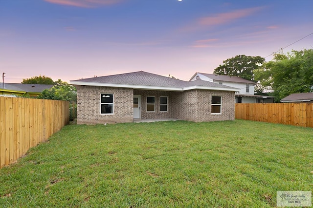 back house at dusk featuring a lawn