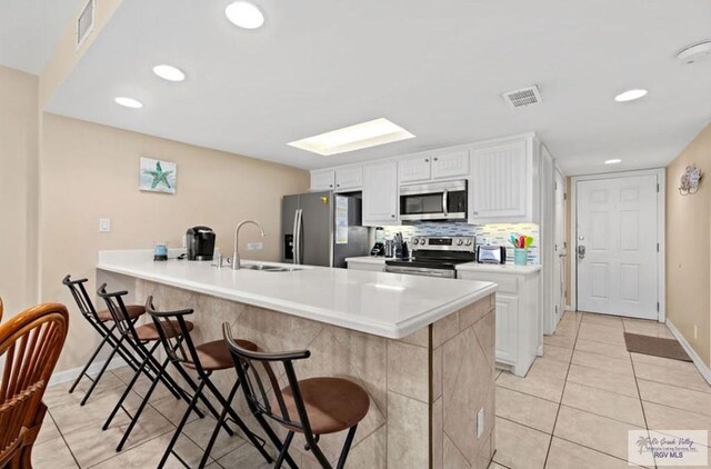 kitchen with stainless steel appliances, light tile patterned floors, kitchen peninsula, a breakfast bar, and white cabinets