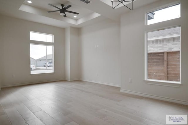 spare room with a tray ceiling, ceiling fan with notable chandelier, and light hardwood / wood-style flooring