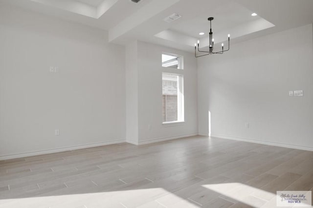 unfurnished room with an inviting chandelier, a tray ceiling, and light hardwood / wood-style floors