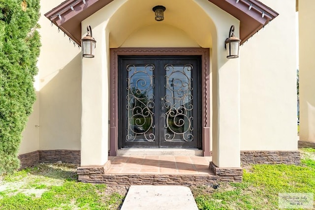 entrance to property featuring stone siding, french doors, and stucco siding