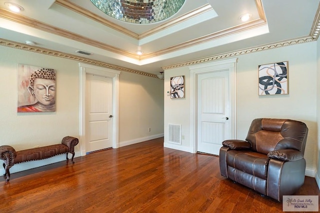 living area with wood finished floors, visible vents, baseboards, ornamental molding, and a raised ceiling