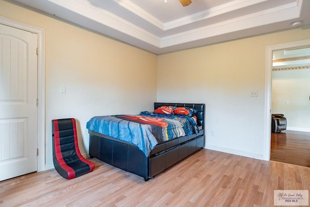 bedroom featuring baseboards, a tray ceiling, wood finished floors, and ornamental molding