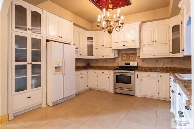 kitchen with light tile patterned floors, white appliances, tasteful backsplash, glass insert cabinets, and an inviting chandelier