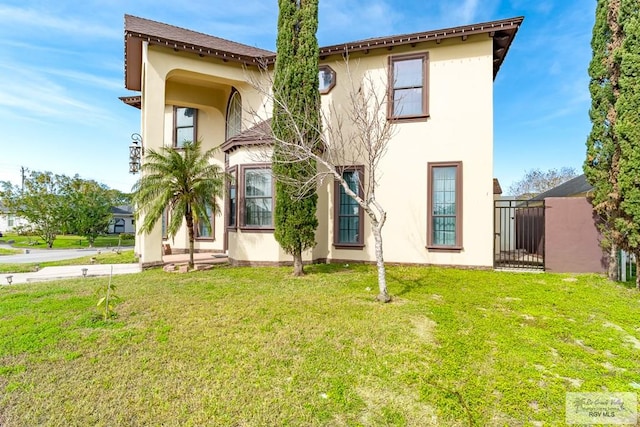 exterior space with a gate, a lawn, and stucco siding