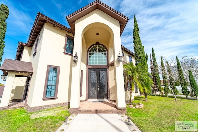 view of exterior entry featuring french doors, a lawn, and stucco siding