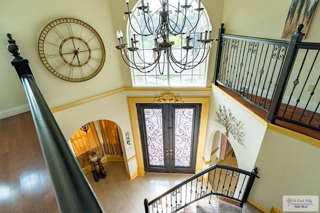 entrance foyer featuring baseboards, arched walkways, stairs, french doors, and a notable chandelier