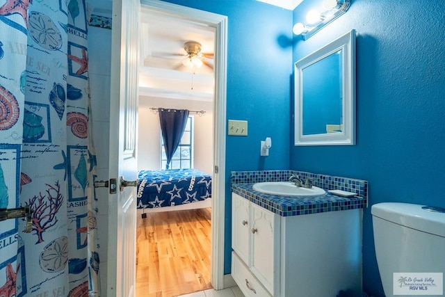 ensuite bathroom with connected bathroom, toilet, wood finished floors, vanity, and a ceiling fan