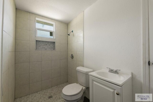 bathroom with a textured ceiling, vanity, a tile shower, and toilet