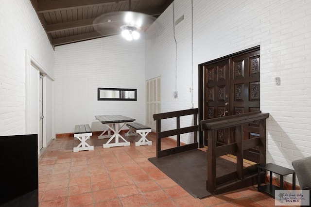 interior space with high vaulted ceiling, beam ceiling, and brick wall