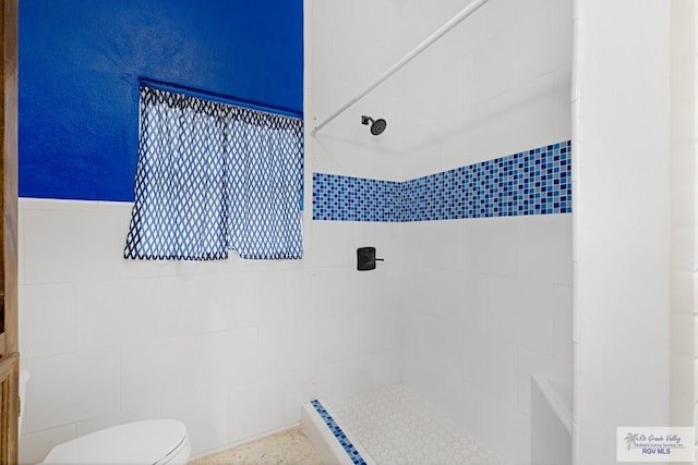 full bath with a tile shower, tile walls, and toilet