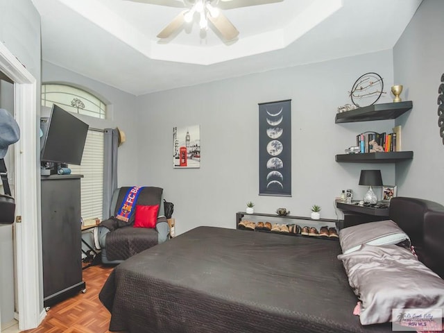 bedroom with light parquet flooring, a raised ceiling, and ceiling fan