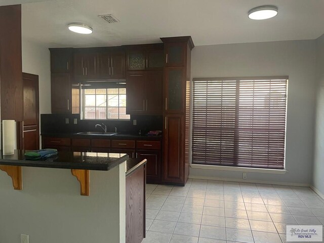 2776 Fleet St, Brownsville, TX 78521 - kitchen with dark countertops, a sink, a kitchen bar, and light tile patterned floors