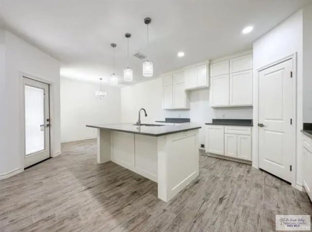 17134 Mandarin Ave, Harlingen, TX 78552 - kitchen with dark countertops, light wood finished floors, white cabinetry, a kitchen island with sink, and a sink