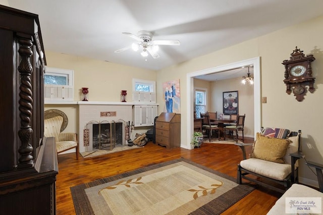 living room featuring ceiling fan with notable chandelier, a fireplace, and dark wood-type flooring