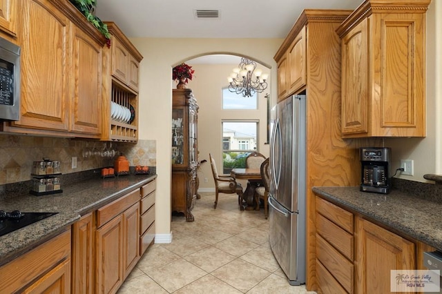 kitchen with decorative backsplash, dark stone counters, stainless steel appliances, a chandelier, and light tile patterned flooring