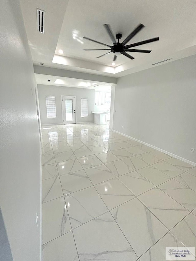 empty room with ceiling fan and a tray ceiling