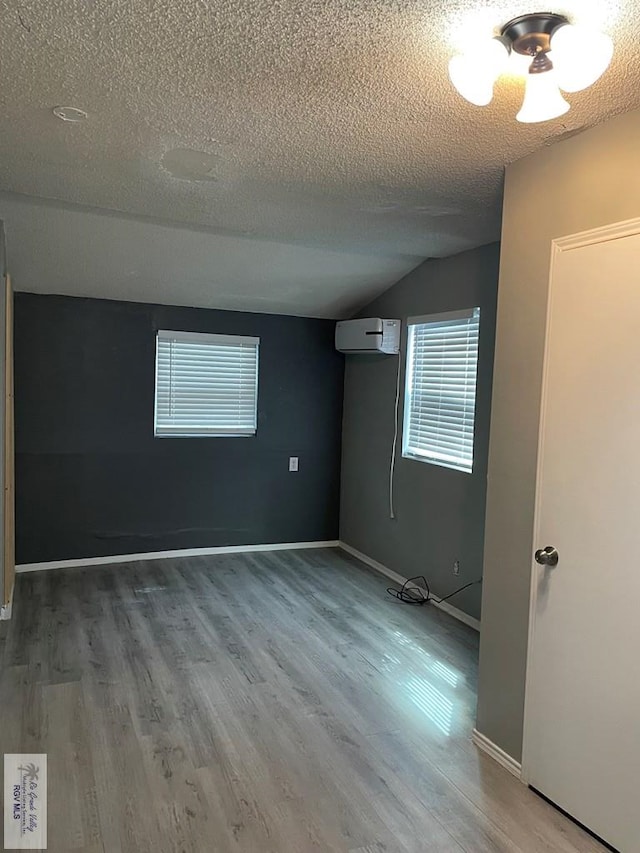 empty room with lofted ceiling, hardwood / wood-style floors, a wall mounted air conditioner, and a textured ceiling