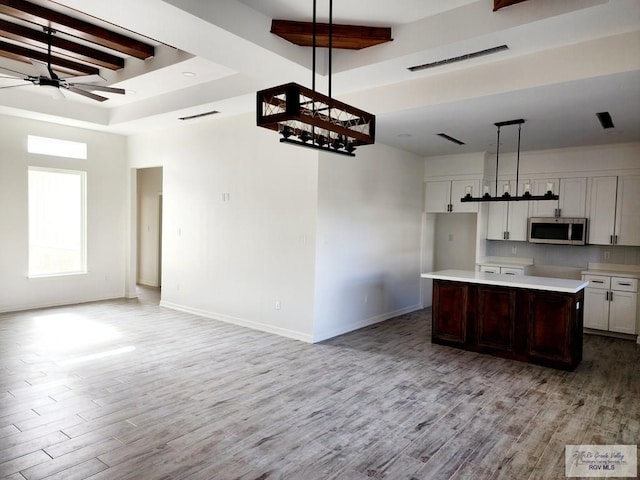 kitchen with ceiling fan, hanging light fixtures, light hardwood / wood-style floors, white cabinets, and a center island with sink