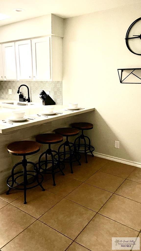 kitchen featuring sink, light tile patterned floors, white cabinetry, backsplash, and a kitchen bar