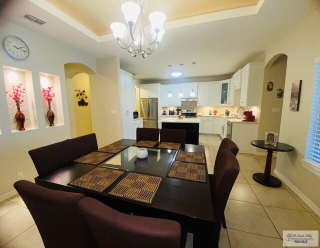 116 Village E Dr, Los Fresnos, TX 78566 - dining space with light tile patterned flooring, arched walkways, a raised ceiling, a chandelier, and baseboards