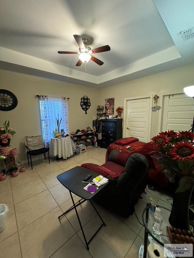 tiled living room with a raised ceiling and ceiling fan