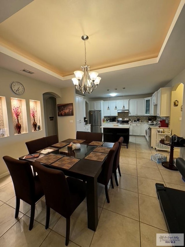 tiled dining area featuring a raised ceiling and an inviting chandelier