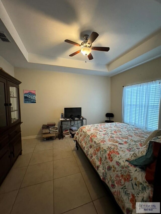 bedroom with ceiling fan, a raised ceiling, and light tile patterned floors