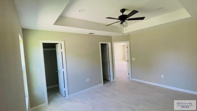 unfurnished bedroom with ceiling fan, a tray ceiling, a closet, and a spacious closet