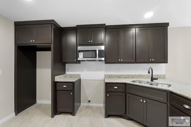 kitchen featuring tasteful backsplash, sink, light stone counters, and dark brown cabinetry