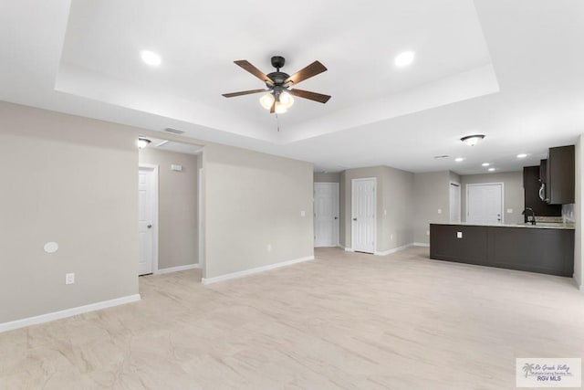 unfurnished living room with ceiling fan, a raised ceiling, and sink