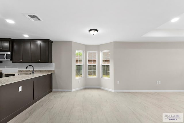 kitchen with dark brown cabinetry, sink, light stone counters, and decorative backsplash