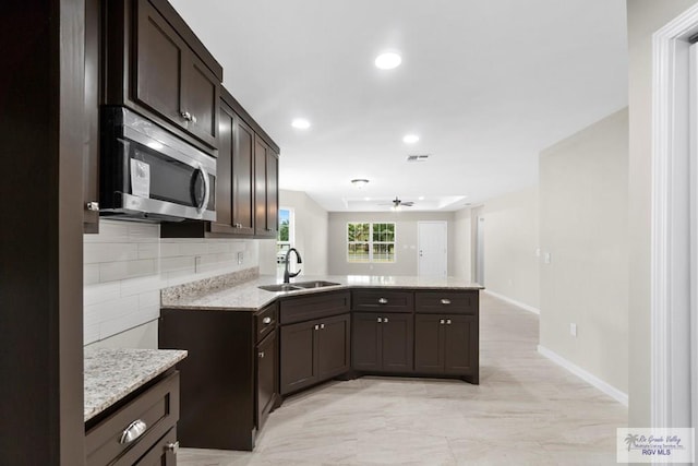 kitchen with sink, backsplash, light stone counters, kitchen peninsula, and dark brown cabinets