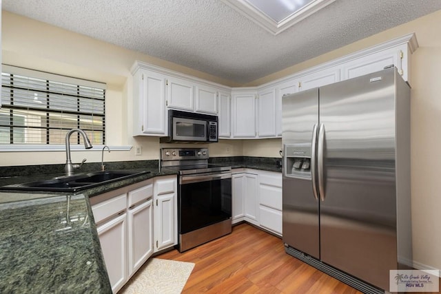 kitchen with a sink, stainless steel appliances, light wood-style floors, a textured ceiling, and white cabinets