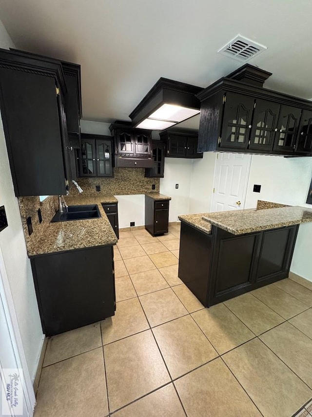 kitchen featuring visible vents, light stone countertops, tasteful backsplash, a sink, and dark cabinets