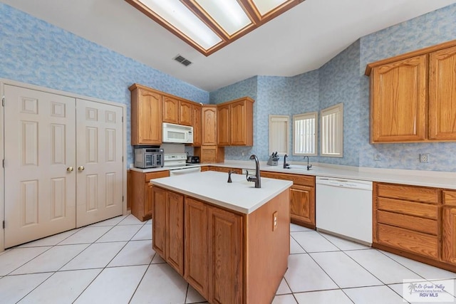 kitchen featuring light tile patterned floors, white appliances, a center island with sink, and sink