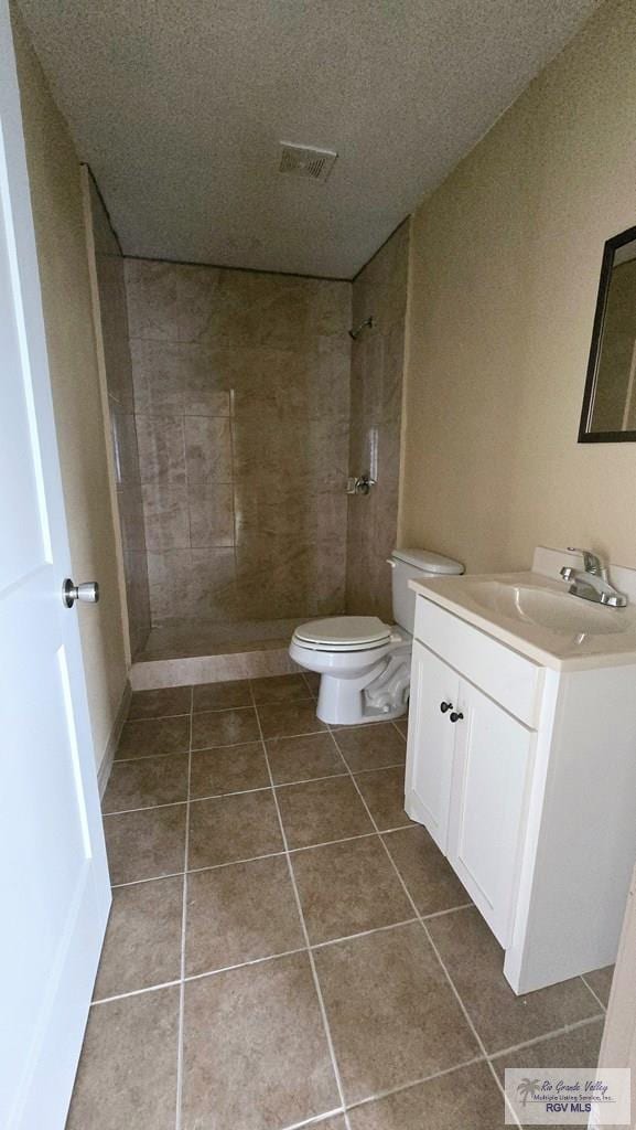 bathroom with tile patterned flooring, a tile shower, vanity, and toilet