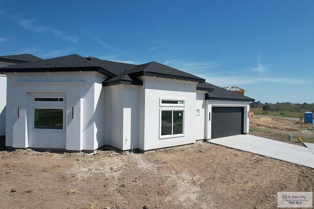 view of front of house featuring an attached garage, stucco siding, concrete driveway, and roof with shingles