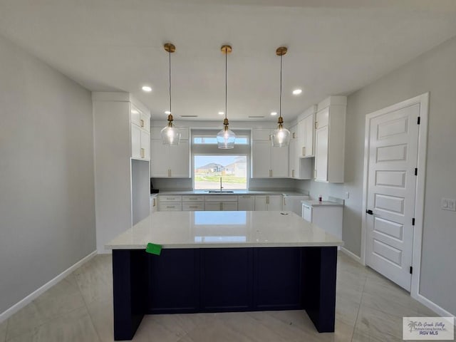 kitchen with baseboards, white cabinetry, a sink, and a center island