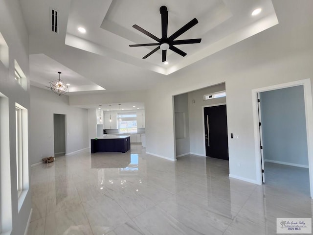 unfurnished living room with visible vents, a high ceiling, a tray ceiling, and baseboards