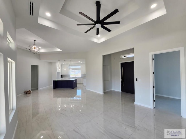 unfurnished living room with baseboards, a high ceiling, visible vents, and a raised ceiling